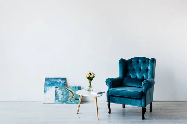 Удобное кресло рядом с тюльпанами на кофейном столике и картины в гостиной — стоковое фото