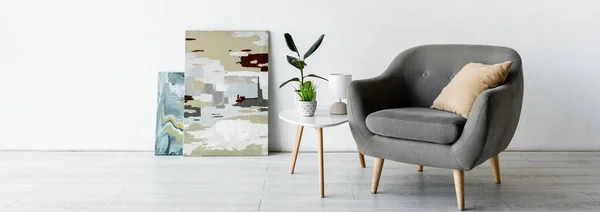 Panoramic crop of comfortable armchair near coffee table with green plants, lamp and paintings in living room — Stock Photo