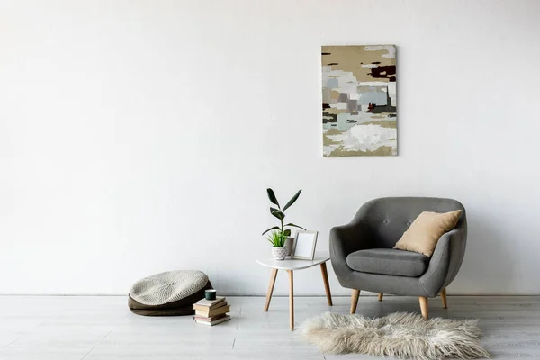 Cómodo sillón cerca de la mesa de centro con plantas verdes, marco y pintura en la pared en la sala de estar moderna - foto de stock