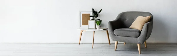 Orientación panorámica de cómodo sillón cerca de mesa de centro con plantas verdes y marcos en la sala de estar moderna - foto de stock