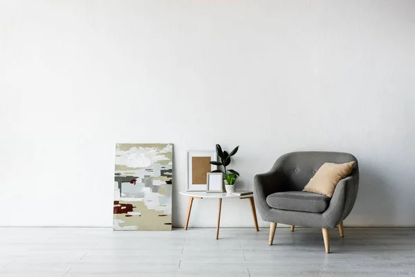 Kissen auf grauem Sessel neben Couchtisch mit grünen Pflanzen und Gestellen im modernen Wohnzimmer — Stockfoto