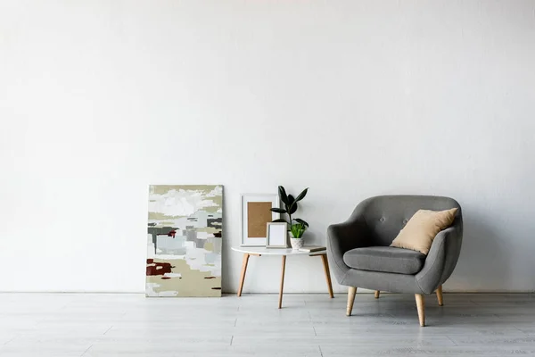 Pillow on grey armchair near coffee table with green plants and frames in modern living room — Stock Photo