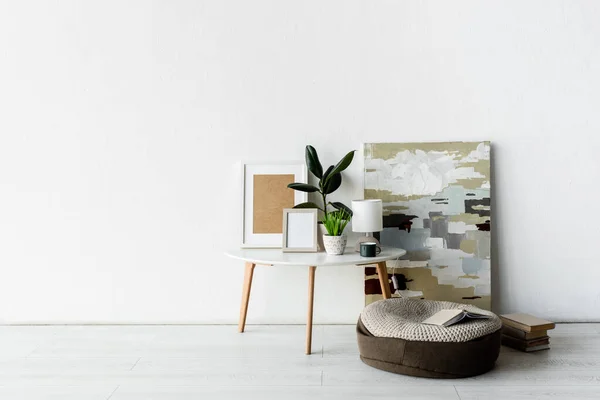 Plantes vertes, cadres et lampe sur table basse blanche près de la peinture et des livres dans un appartement moderne — Photo de stock