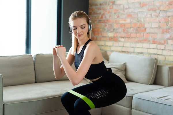 Sportive woman in wireless headphones doing squat exercise at home — Stock Photo