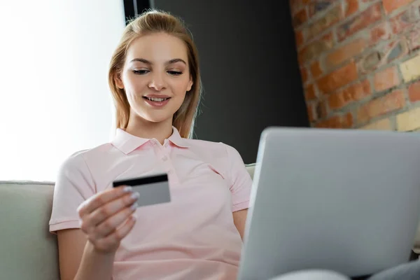 Enfoque selectivo de la chica feliz mirando la tarjeta de crédito cerca de la computadora portátil - foto de stock