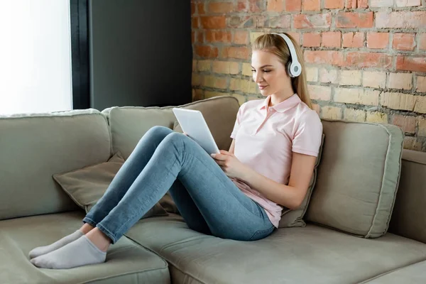 Cheerful woman in wireless headphones using digital tablet in living room — Stock Photo