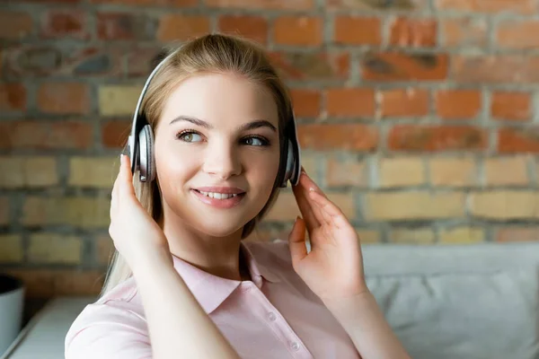 Young smiling woman touching wireless headphones at home — Stock Photo
