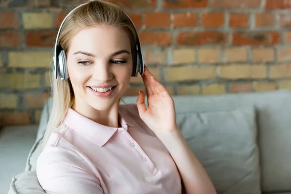 Smiling woman touching wireless headphones at home — Stock Photo