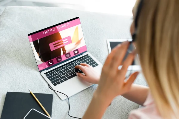 Enfoque selectivo de freelancer tocando auriculares cerca de la computadora portátil con entradas en línea sitio web y tableta digital con pantalla en blanco en la cama - foto de stock