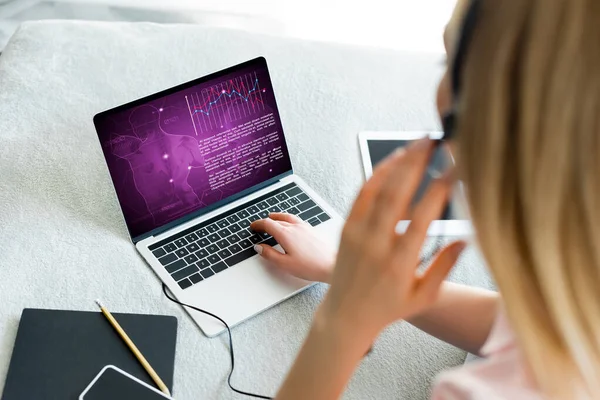 Selective focus of freelancer touching headset near laptop with medical tracker and digital tablet with blank screen on bed — Stock Photo