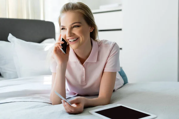 Mujer feliz hablando en el teléfono inteligente y la celebración de la tarjeta de crédito cerca de la tableta digital con pantalla en blanco en el dormitorio - foto de stock