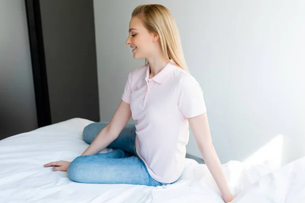 Profil des hübschen und lächelnden Mädchens, das zu Hause auf dem Bett sitzt — Stockfoto