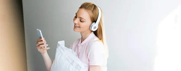 Panoramic shot of smiling woman in wireless headphones using smartphone at home — Stock Photo