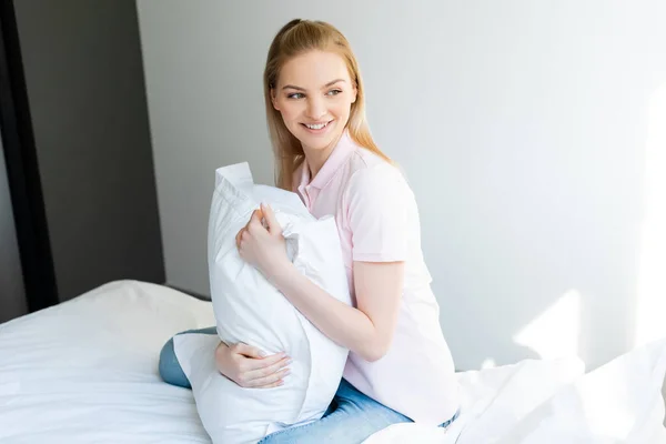 Mujer bonita y sonriente sentada en la cama y mirando hacia otro lado - foto de stock