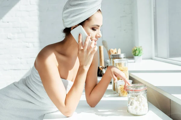 Side view of sexy girl in towels talking on smartphone near kitchen worktop — Stock Photo