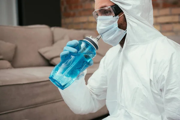 Hombre en traje de materiales peligrosos, máscara médica y gafas de agua potable mientras sostiene la botella de deportes - foto de stock