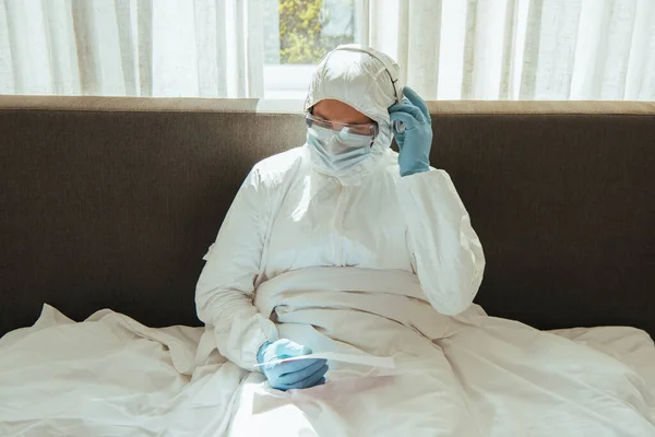 Mann in persönlicher Schutzausrüstung hält Papier und berührt Kopfhörer im Schlafzimmer — Stockfoto
