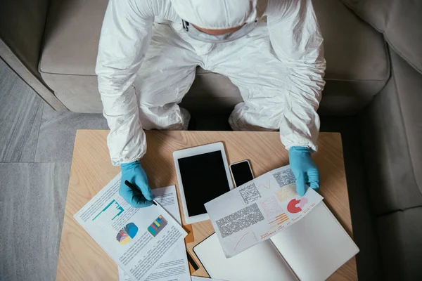 Vue de dessus de l'homme en équipement de protection individuelle travaillant près de tablette numérique, graphiques et graphiques et smartphone avec écran blanc — Photo de stock