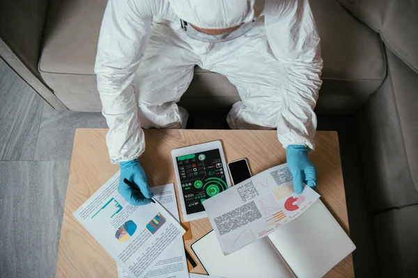 Top view of man in personal protective equipment working near digital tablet with charts and graphs and smartphone with blank screen — Stock Photo