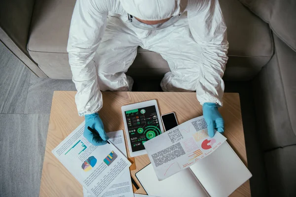 Vue de dessus de l'homme en équipement de protection individuelle travaillant près de tablette numérique avec des graphiques et des graphiques et smartphone avec écran blanc — Photo de stock