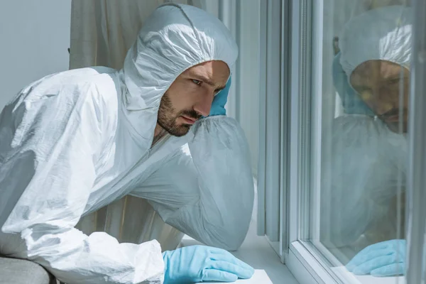 Triste homme barbu en équipement de protection individuelle regardant la fenêtre — Photo de stock