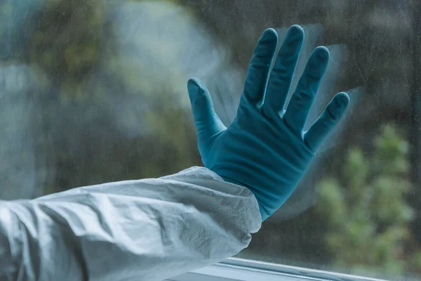 Vista recortada del hombre en guante de látex tocando ventana, concepto de cuarentena - foto de stock