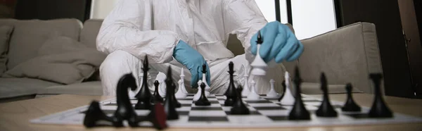 Panoramic shot of man in personal protective equipment and medical mask playing chess — Stock Photo