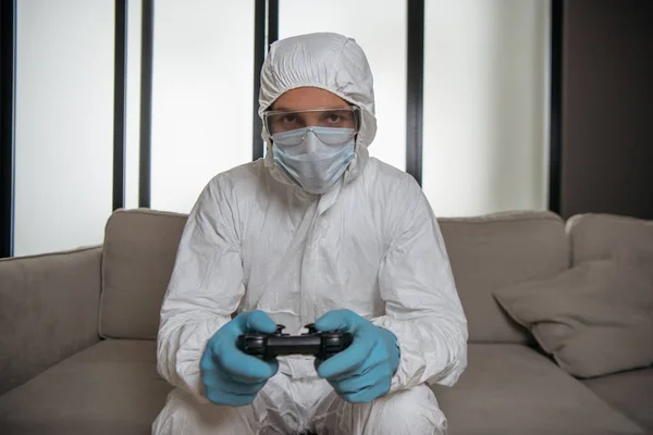 KYIV, UCRÂNIA - ABRIL 11, 2020: homem em equipamentos de proteção individual e máscara médica jogando videogame — Fotografia de Stock