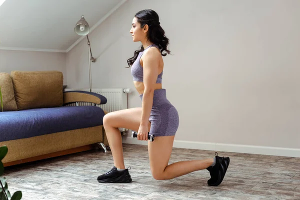 Attraktives sportliches Mädchen, das zu Hause mit Kurzhanteln Ausfallschritte macht — Stockfoto