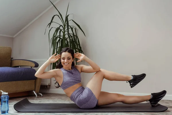 Счастливая спортивная девушка делает пресс и тренировки на фитнес коврик дома во время самоизоляции — стоковое фото