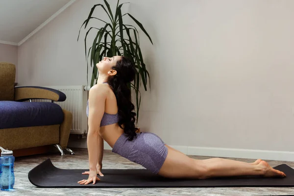 Attraktives sportliches Mädchen, das während der Selbstisolierung zu Hause auf einer Yogamatte übt — Stockfoto