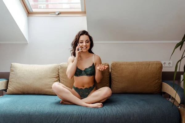 Attractive sexy girl in lingerie talking on smartphone while sitting on sofa at home — Stock Photo