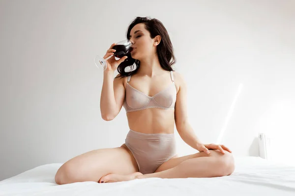 Menina sedutora em lingerie segurando copo de vinho tinto em casa durante o auto-isolamento — Fotografia de Stock