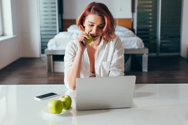 Glückliches Mädchen im Gespräch beim Apfel essen, während es zu Hause Laptop auf Selbstisolierung benutzt — Stockfoto