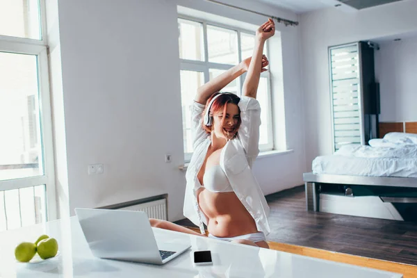 Happy girl in headphones using laptop and smartphone at home on self isolation — Stock Photo