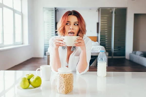 Attraente ragazza leccare cornflakes con latte per la prima colazione durante la quarantena — Foto stock
