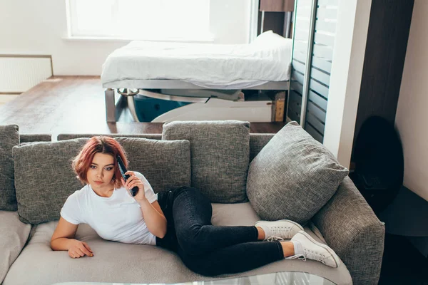 Chica aburrida con mando a distancia viendo la televisión en casa en auto aislamiento - foto de stock