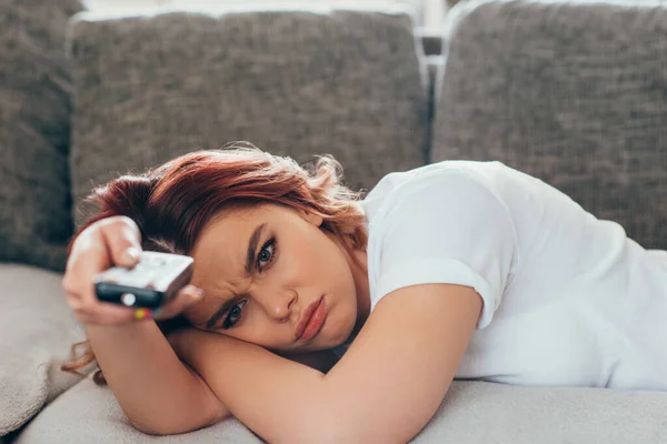 Angry girl with remote controller watching tv at home on quarantine — Stock Photo