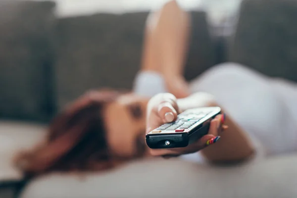 Self isolation of girl with remote controller watching tv while lying on sofa during self isolation — Stock Photo