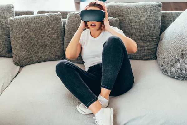 Chica sorprendida usando auriculares de realidad virtual en casa en cuarentena - foto de stock