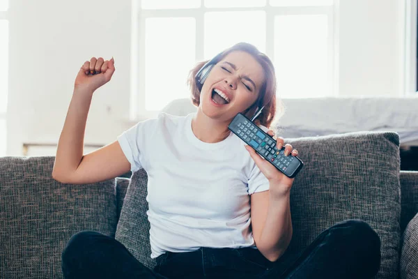 Excited girl in headphones singing with remote controller at home during self isolation — Stock Photo