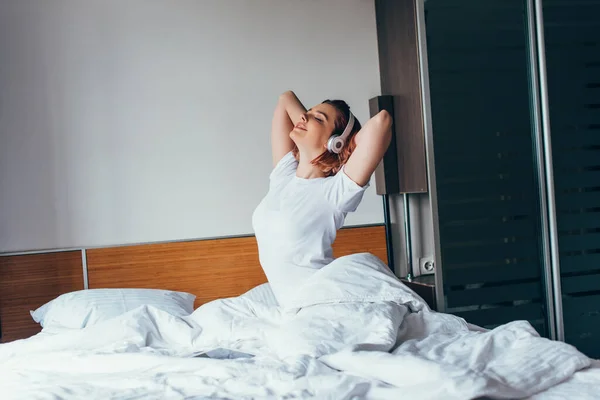 Menina feliz ouvir música com fones de ouvido na cama durante o auto-isolamento — Fotografia de Stock