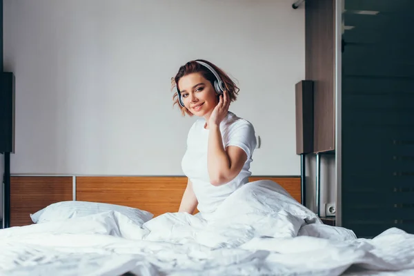 Lächelndes Mädchen, das während der Quarantäne Musik mit Kopfhörern im Bett hört — Stockfoto