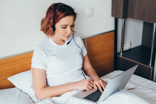 Beautiful girl making video call with headset and laptop in bed during quarantine — Stock Photo