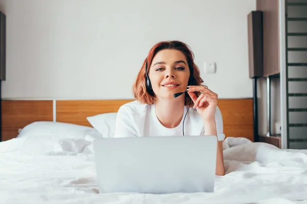 Lächelndes Mädchen beim Videoanruf mit Headset und Laptop im Bett während der Selbstisolation — Stockfoto