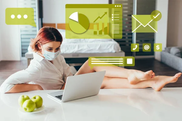 Barefoot freelancer in medical mask working on laptop at home with apples on self isolation with business graphics — Stock Photo