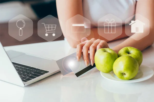 Abgeschnittene Ansicht einer Frau beim Online-Shopping mit Laptop und Kreditkarten auf Küche mit Äpfeln während der Selbstisolation mit Einkaufsschildern — Stockfoto
