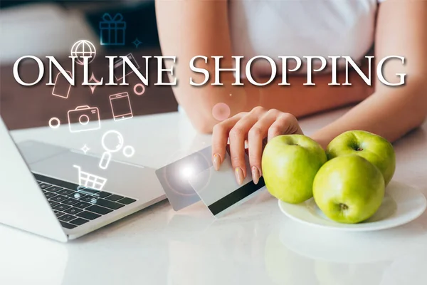 Cropped view of woman with laptop holding credit cards on kitchen with apples during self isolation with online shopping lettering and signs — Stock Photo