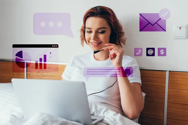 Smiling freelancer making video call with headset and laptop in bed during quarantine with business signs — Stock Photo