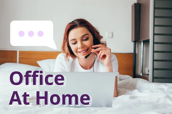Bella felice freelance fare videochiamate con auricolare e laptop a letto durante l'isolamento con ufficio a casa lettering — Foto stock